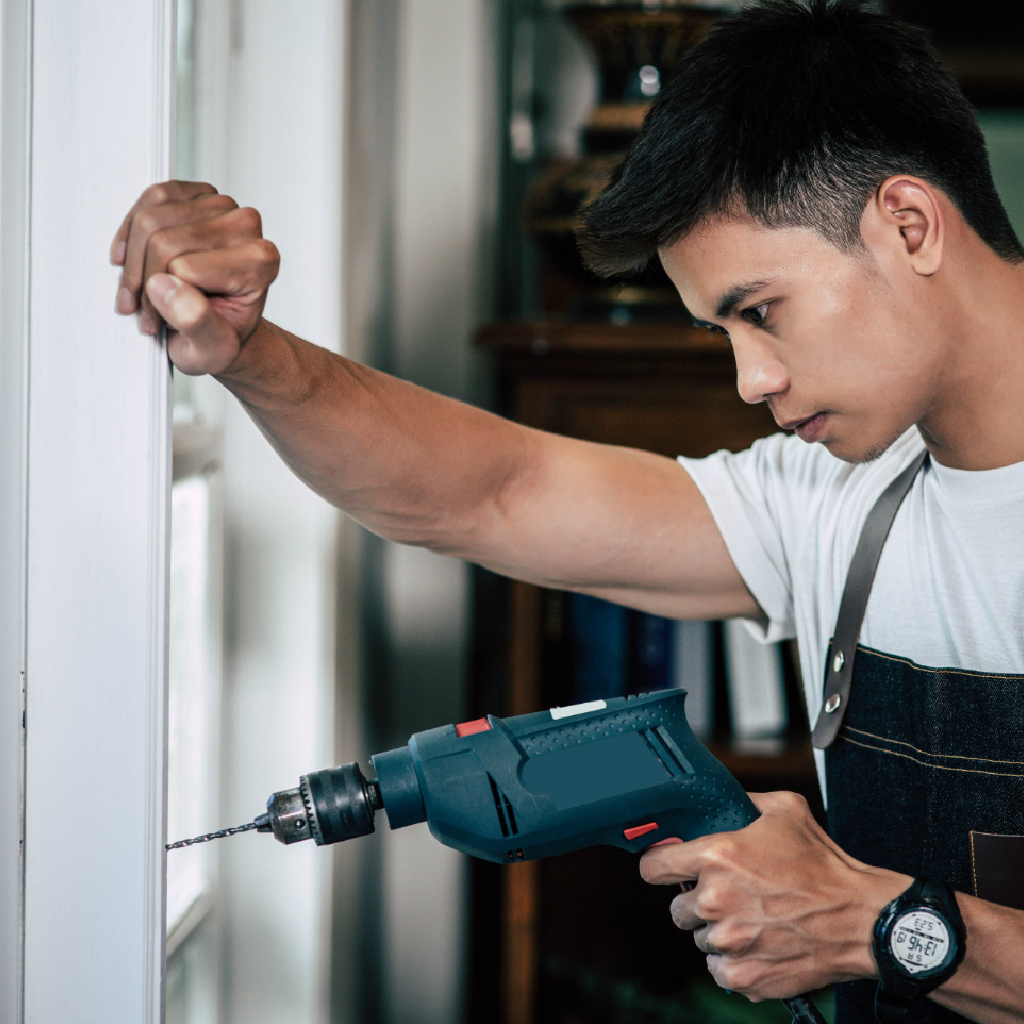 The carpenter holds the drill and drills the window.